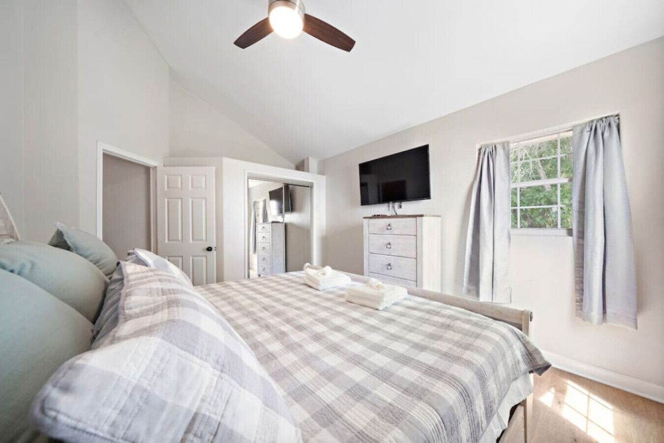 A bedroom with a bed, a dresser, a television, and a window with curtains.
