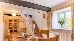 Ein Essbereich mit einem Holztisch, gedeckt für vier Personen, einer Treppe und einem Fenster mit Vorhängen.