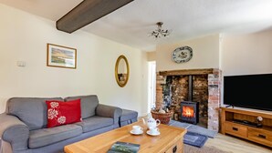 Ein gemütliches Wohnzimmer mit grauem Sofa, einem Holztisch, einem Kamin und einem Fernseher.