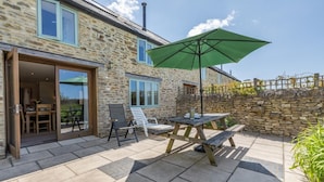 Ein Steinhaus mit einer Terrasse, ausgestattet mit Tisch, Stühlen und einem Sonnenschirm.
