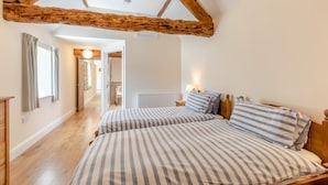 Ein Schlafzimmer mit zwei Betten, Holzbalken an der Decke, einem Heizkörper und einem Gang zu einem anderen Raum.