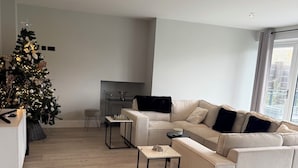 Una sala de estar moderna con un sofá seccional beige grande, una mesita auxiliar y un árbol de Navidad.