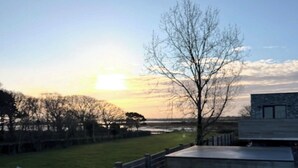 Dos tazas sobre un repisa de madera con vista a un atardecer y un árbol al fondo.