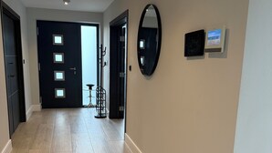 Un pasillo con suelo de madera, una puerta negra con paneles de vidrio, un espejo redondo y un reloj de pared.