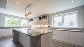 Una cocina moderna con una isla grande, iluminación colgante y ventanas amplias.