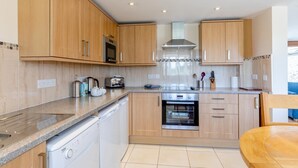 A modern kitchen with wooden cabinets, stainless steel appliances, and a dishwasher. - 3 Bed in Burton Bradstock (oc-c30571) (Burton Bradstock)