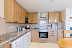 A modern kitchen with wooden cabinets, stainless steel appliances, and a dishwasher. - 3 Bed in Burton Bradstock (oc-c30571) (Burton Bradstock)