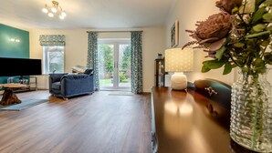 Ein Wohnzimmer mit einer Couch, einem Fernseher, einer Lampe und einer Vase mit Blumen.