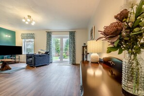 A living room with a sofa, a TV, a lamp, and a vase with flowers. - 2 Bed in Kilgetty (oc-s30541) (Saundersfoot)