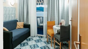 A compact room with a blue sofa, a small table with a chair, and a view of the sea through a window. - 1 bedroom stunning apartment in Klek (Klek)