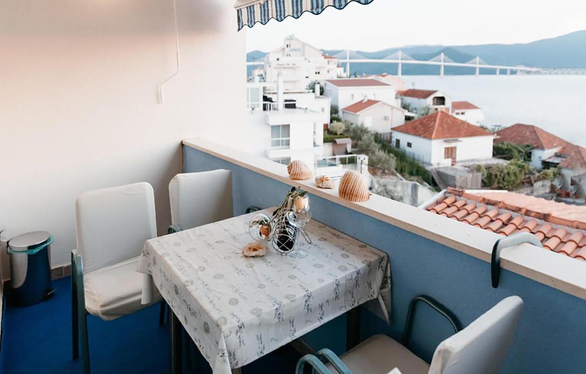 Un balcón con una mesa para dos, con vistas a un pueblo costero de edificios blancos y un puente a lo lejos.