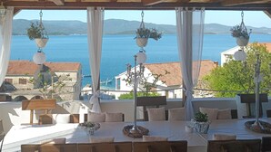 A terrace with a table set for dining, overlooking a coastal view with hanging plants and a clear sky. - 1 bedroom stunning apartment in Klek (Klek)