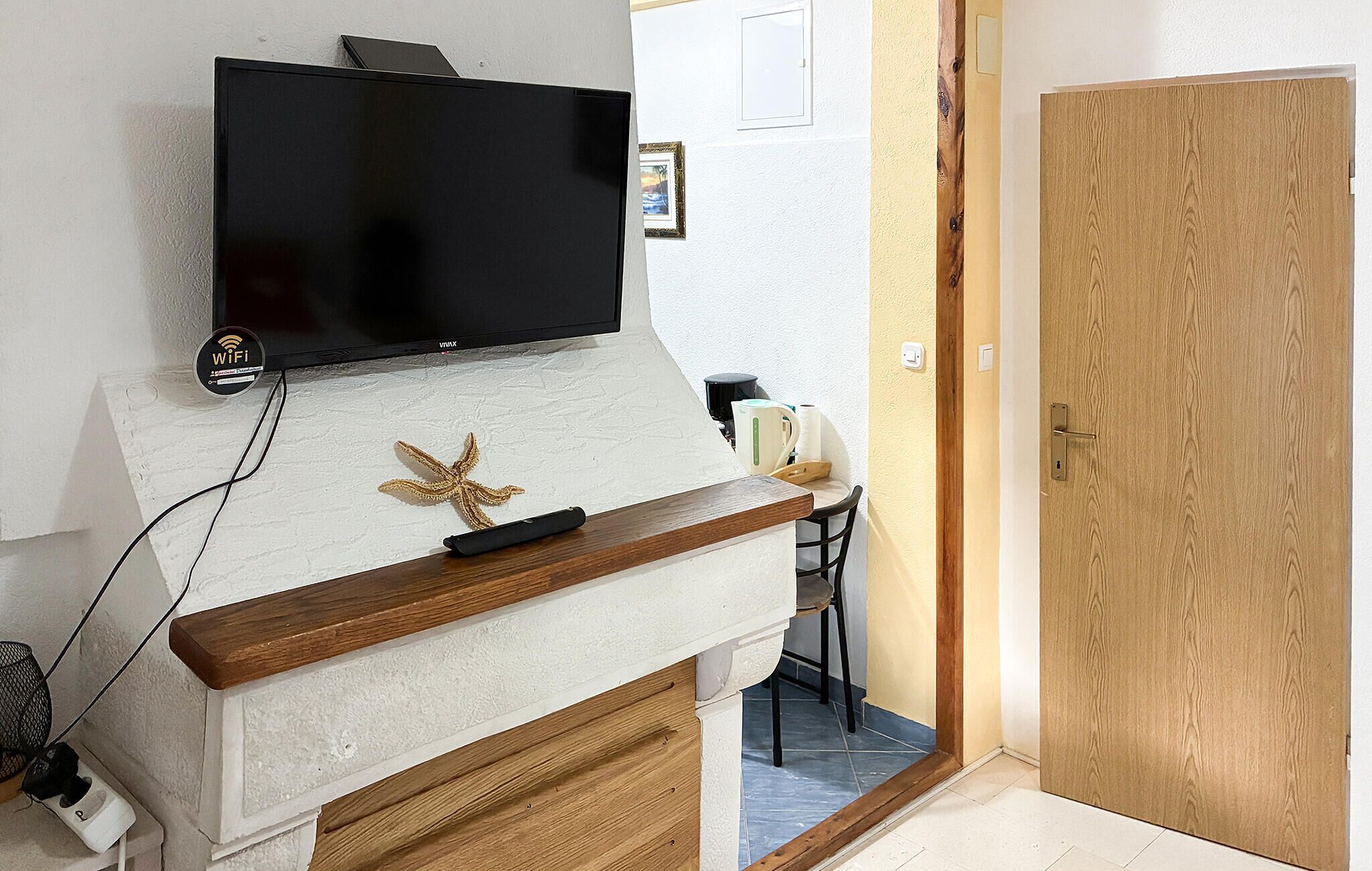 A modern living room with a flat-screen TV mounted on a white textured wall, a wooden coffee table, and a starfish decoration.