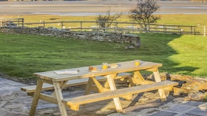 A picnic table with food and drinks, set against a scenic backdrop of mountains and a lake. - 8 Bed in Ynys (oc-c29818) (Ynys)