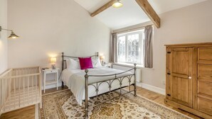A bedroom with a metal bed frame, a wooden wardrobe, a window with curtains, a bedside table with a lamp, and a patterned rug. - 8 Bed in Ynys (oc-c29818) (Ynys)