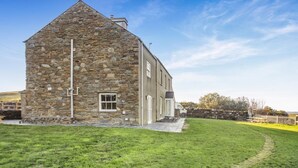 A stone building with a sloped roof, a small window, and a paved driveway leading to the entrance. - 8 Bed in Ynys (oc-c29818) (Ynys)