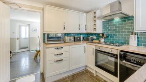 A modern kitchen with white cabinets, a microwave, a toaster, a stove, and a green-tiled backsplash.