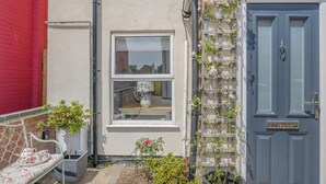 A building with a blue door, a window with a white frame, and a small garden area with a bench and potted plants.
