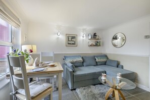 A modern living room with a grey sofa, a dining table with chairs, a glass coffee table, and a fluffy rug.
