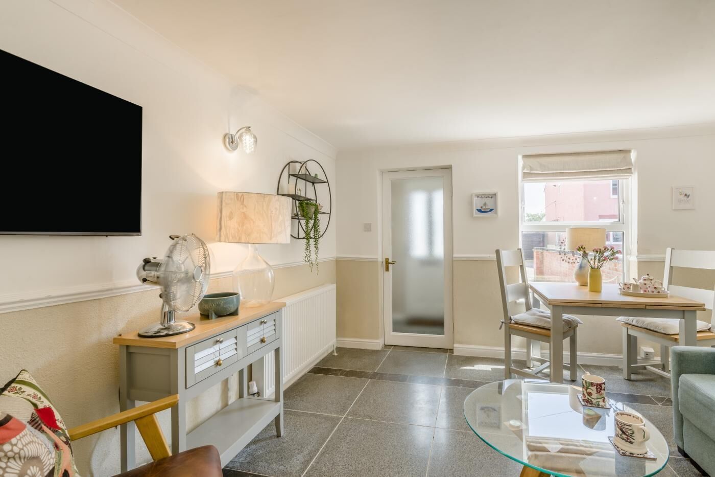 Un soggiorno moderno con televisore, ventilatore, lampada, tavolo da pranzo con sedie e tavolino in vetro.
