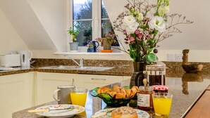 Une cuisine équipée d’un coin petit-déjeuner comprenant des croissants, un panier de fruits et une machine à café.