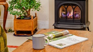 Une pièce chaleureuse avec une table en bois, une plante en pot, un magazine, une tasse et un poêle à bois.