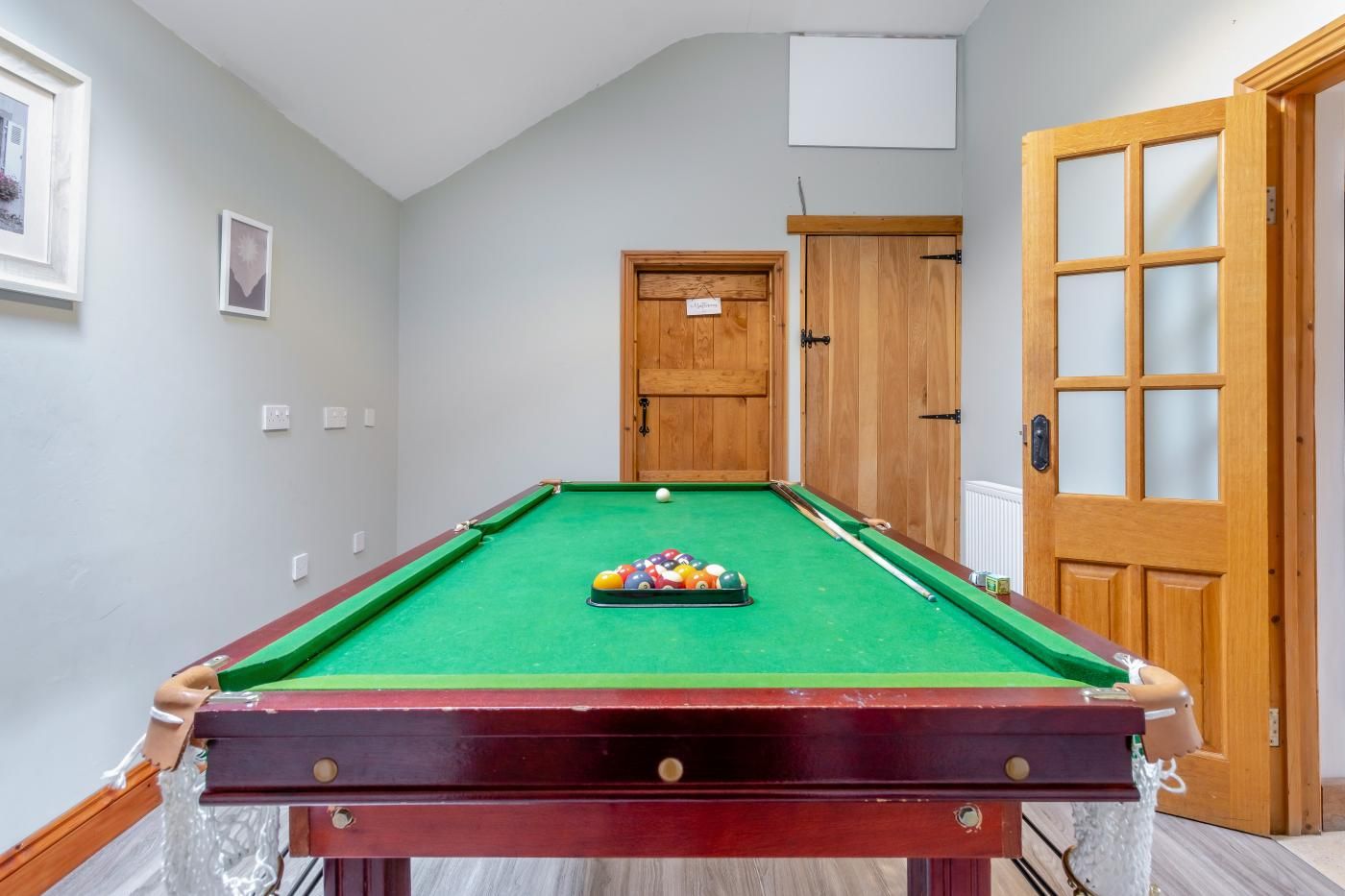 Een pooltafel met ballen en stokken, een houten deur en een lijst met een foto aan de muur.