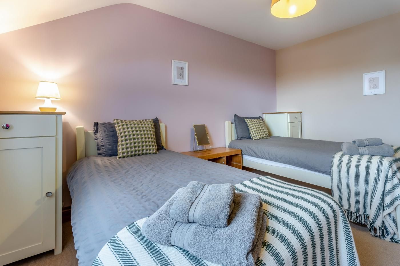 A bedroom with two beds, a bedside table, a lamp, and a wardrobe.