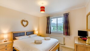 Camera d'albergo con un letto, lampade da comodino, una decorazione a forma di cuore, una finestra con tende e una televisione su un mobile in legno.