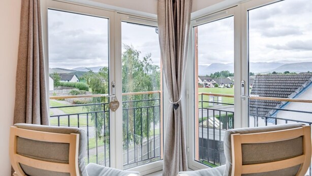 Un balcone con due sedie, una porta vetrata e vista su una zona residenziale con case e spazi verdi.