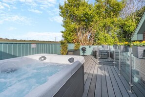 Ein Whirlpool auf einer Holzterrasse mit Grill und Gartenmöbeln.