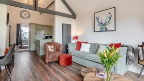 Ein modernes Wohnzimmer mit einem grauen Sofa, roten Kissen, einem roten Hocker und einem Holztisch mit einem Blumenstrauß.