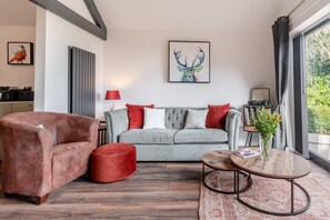 Ein modernes Wohnzimmer mit einem grauen Sofa, roten Kissen, einem rosafarbenen Sessel, einem runden Couchtisch und einem großen Fenster mit Vorhängen.