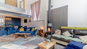 A modern living room with a fireplace, a sofa, a coffee table, and a kitchen area with bar stools. - 3 Bed in Crowle (oc-s30617) (Crowle)