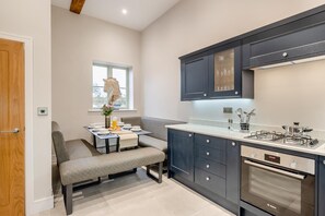 A modern kitchen with a built-in oven, a dining area with a bench, and a window with a view. - 4 Bed in Wellesbourne (oc-t30595) (Wellesbourne)