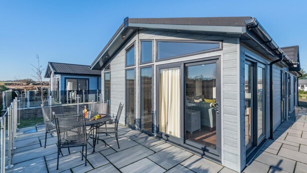 Ett modernt hus med ett glashus, en uteplats med utemöbler och utsikt över det omgivande landskapet.