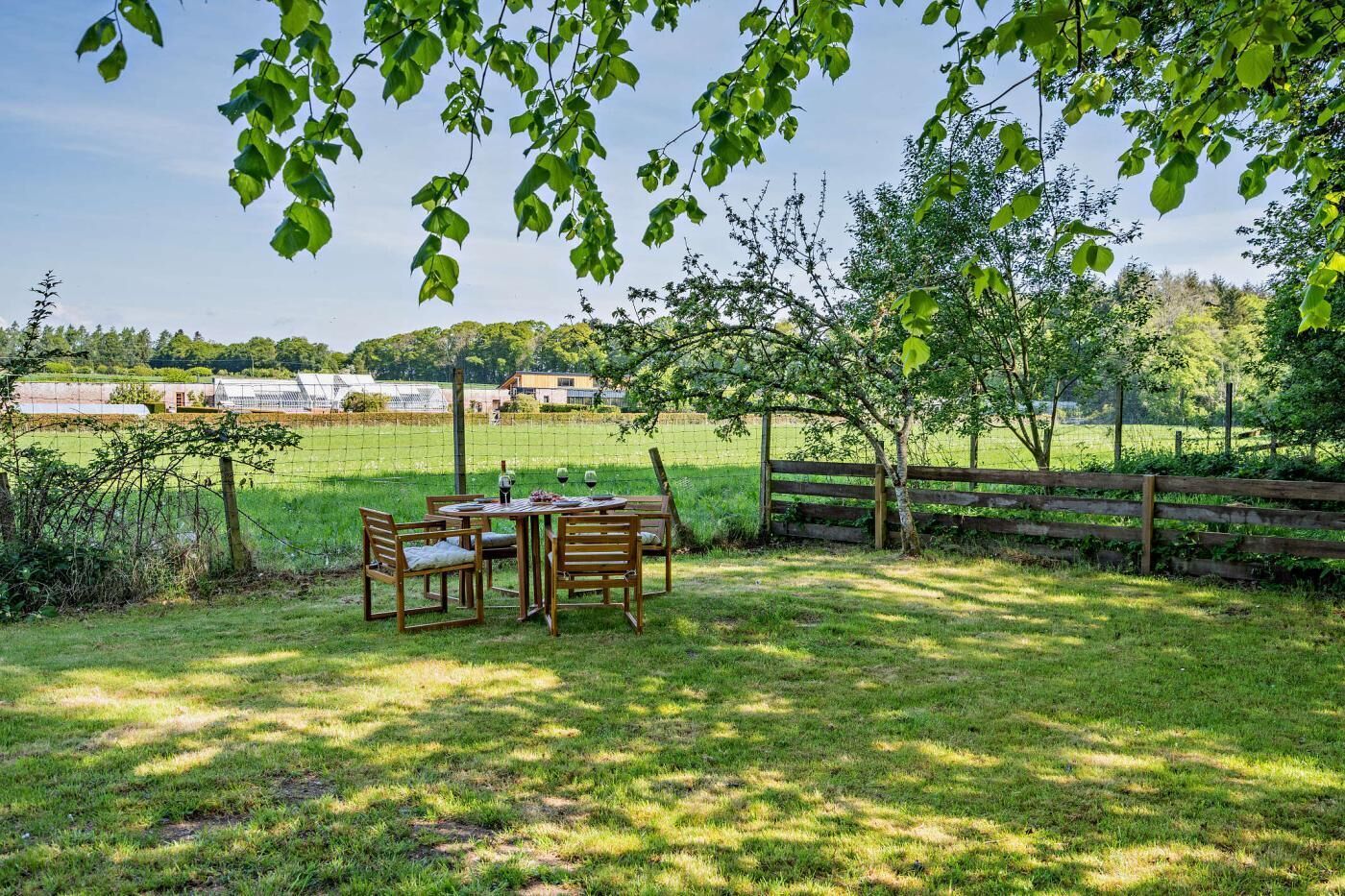 Un área de comedor al aire libre con una mesa y sillas, rodeada por una valla de madera y árboles.