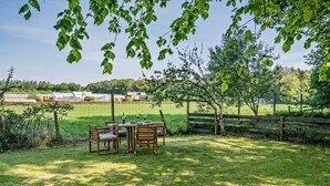 Un espace extérieur aménagé pour les repas, avec une table et des chaises, entouré d’une clôture en bois et d’arbres.