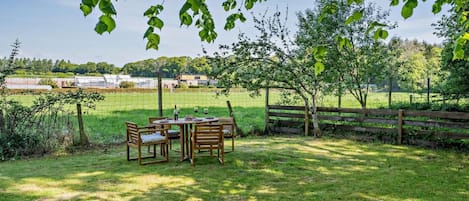 An outdoor dining area with a table and chairs, surrounded by a wooden fence and trees.