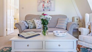 Un salon avec un canapé, une table basse ornée d’un vase de fleurs, un tableau encadré au mur et une table d’appoint avec une lampe.