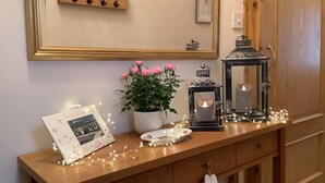 Une console en bois ornée d’une photo encadrée, d’une plante en pot aux fleurs roses, de deux lanternes et de guirlandes lumineuses.