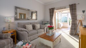 Un salon chaleureux avec un canapé, une table basse et un grand miroir. Il y a une fenêtre avec des rideaux et une vue sur l’extérieur.