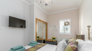 Une chambre à coucher avec un lit, une télévision, un miroir, une fenêtre et un lustre.