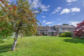 A stone house with a well-maintained lawn, a conservatory, and a large tree with red leaves. - 2 Bed in Rosyth (oc-r30512) (Rosyth)