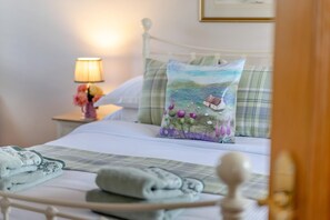 A neatly made bed with a pillow featuring a landscape design, a bedside lamp, and a framed picture on the wall. - 2 Bed in Rosyth (oc-r30512) (Rosyth)