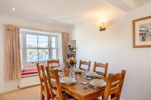 Ein Esszimmer mit Holztisch, gedeckt für vier Personen, einer Blumenvase und Meerblick durch große Fenster.