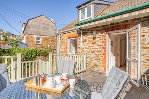 A glass-top table with a tray of breakfast items, a stone building with a brick facade, and a white fence. - 3 Bed in Polruan (oc-g30535) (Fowey)