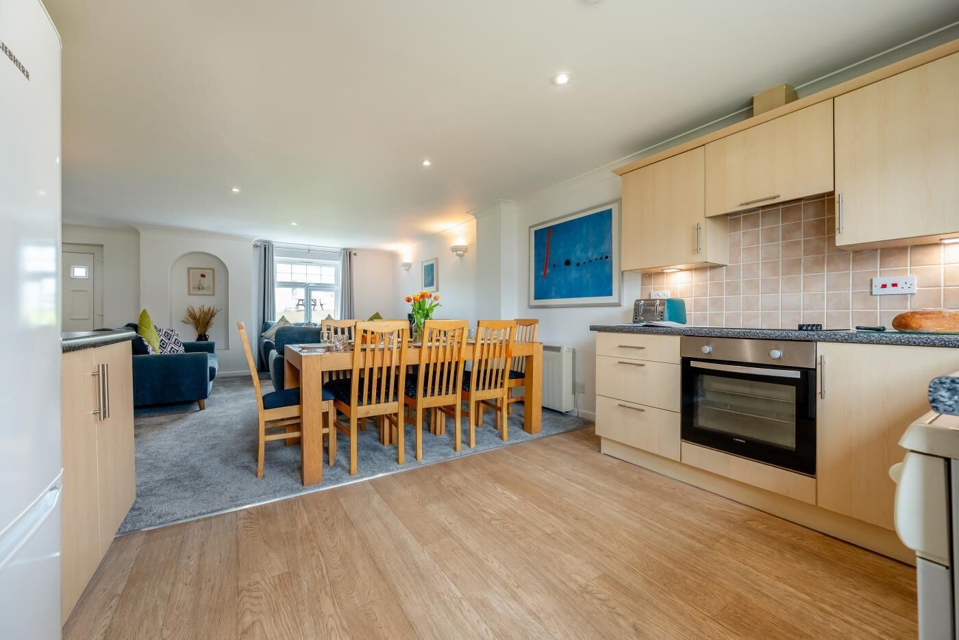 A modern kitchen with wooden cabinets, a built-in oven, and a dining area with a wooden table and chairs.