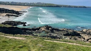 Paisagem costeira com um litoral rochoso, uma praia arenosa e uma vista clara do mar.