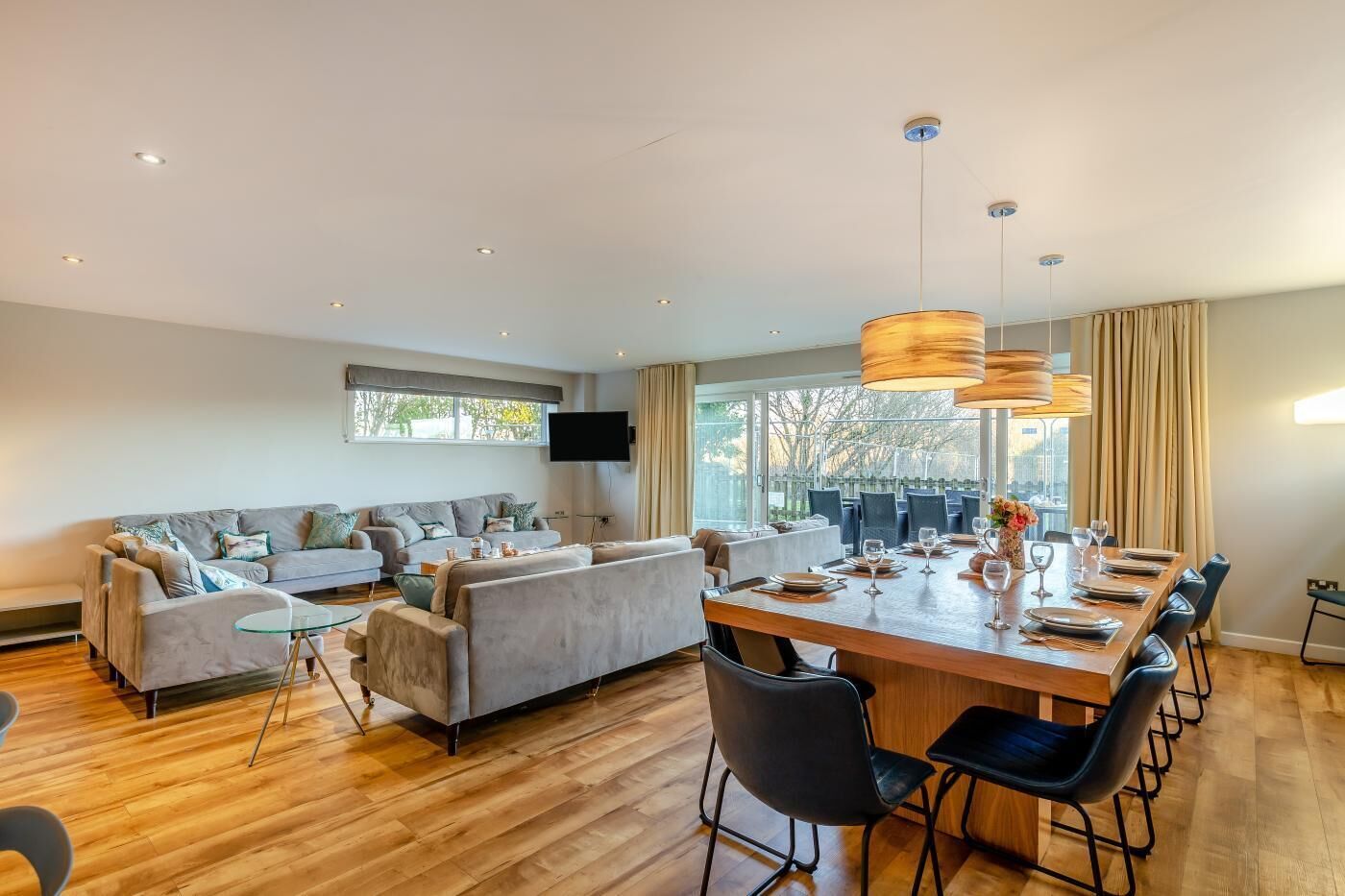 A modern living room with a sofa set, a dining table with chairs, and a TV mounted on the wall.